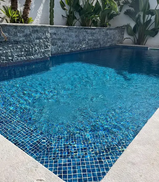 Piscine carrelée mosaïque bleue avec mur d'eau ardoise et végétation tropicale — Île-de-France